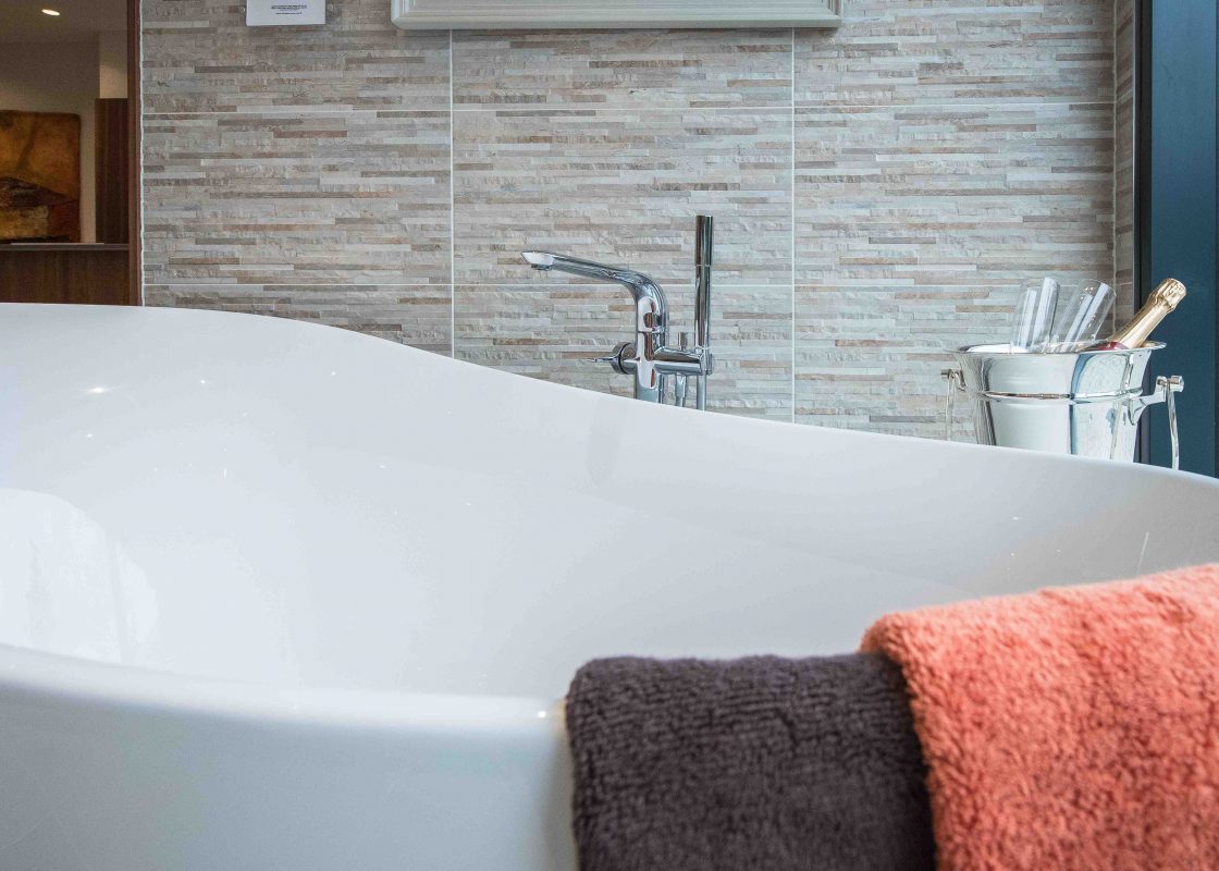 A close up of a ceramic curved bath tub with towels and a bottle of champagne