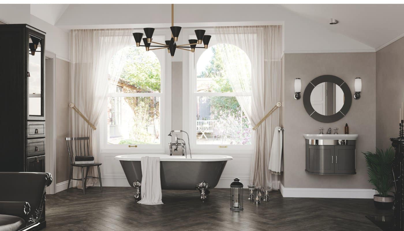 This picture shows a dark-finish freestanding bath from Imperial Bathroom, a black chandelier with brass, and a dark grey mounted vanity unit with a round mirror above.