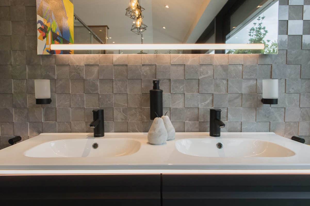 A dual ceramic wash basin with wall mounted mirror and square wall tiles