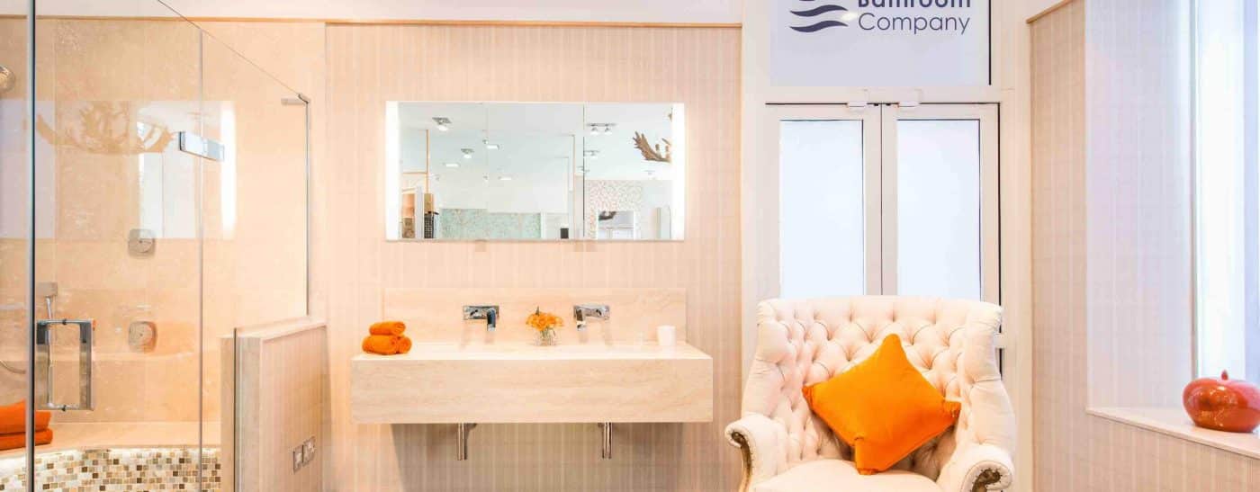 Peach coloured tiles, armchair, large open showering area, wall mounted rectangular mirror and sink