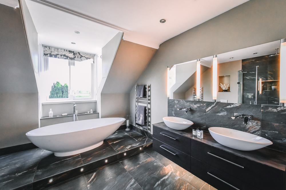 A black marble tiled bathroom with an oval free standing ceramic bath