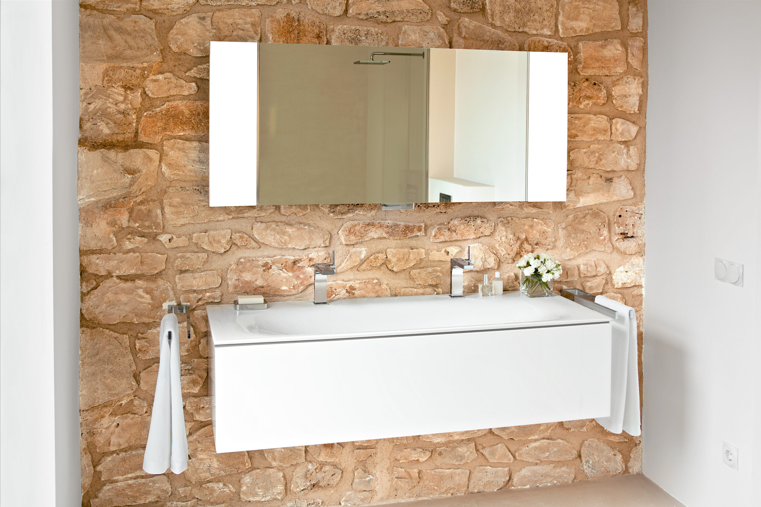 A wall-mounted vanity unit in a matte white finish with large mirror cabinets above it.