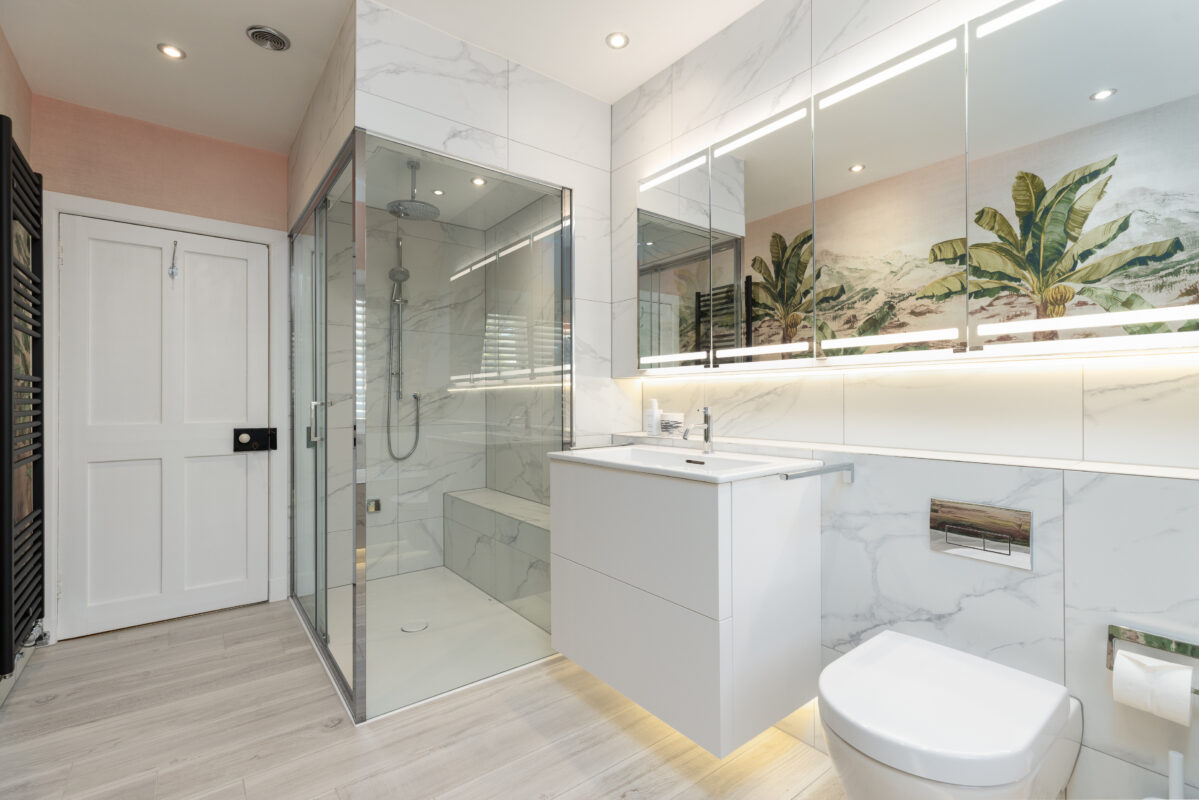A bathroom renovation in Edinburgh integrated with a steam room. The space features a large mirrored cabinet with lighting, a vanity unit in white finish, and a WC.