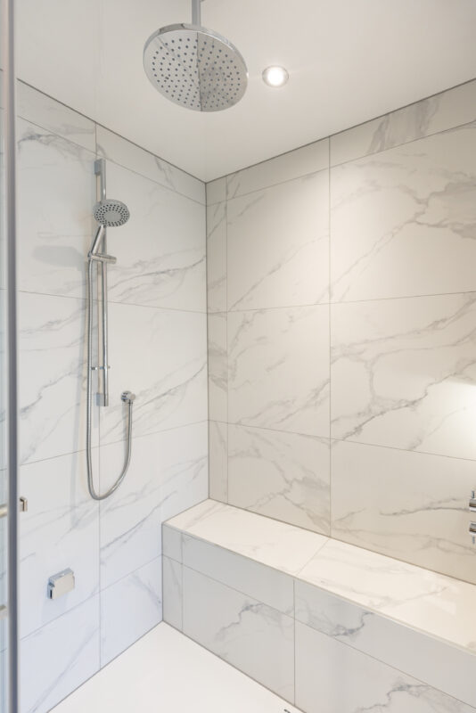 A steam room featuring a chrome shower system with an overhead rain shower.