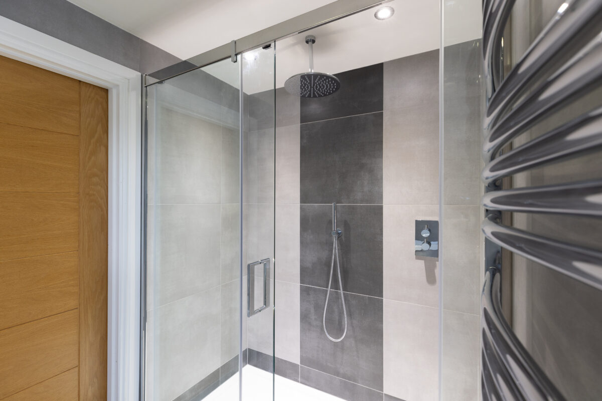 A spacious shower area equipped with a shower panel. The shower area showcases chrome fixtures and a ceiling-mounted shower head.