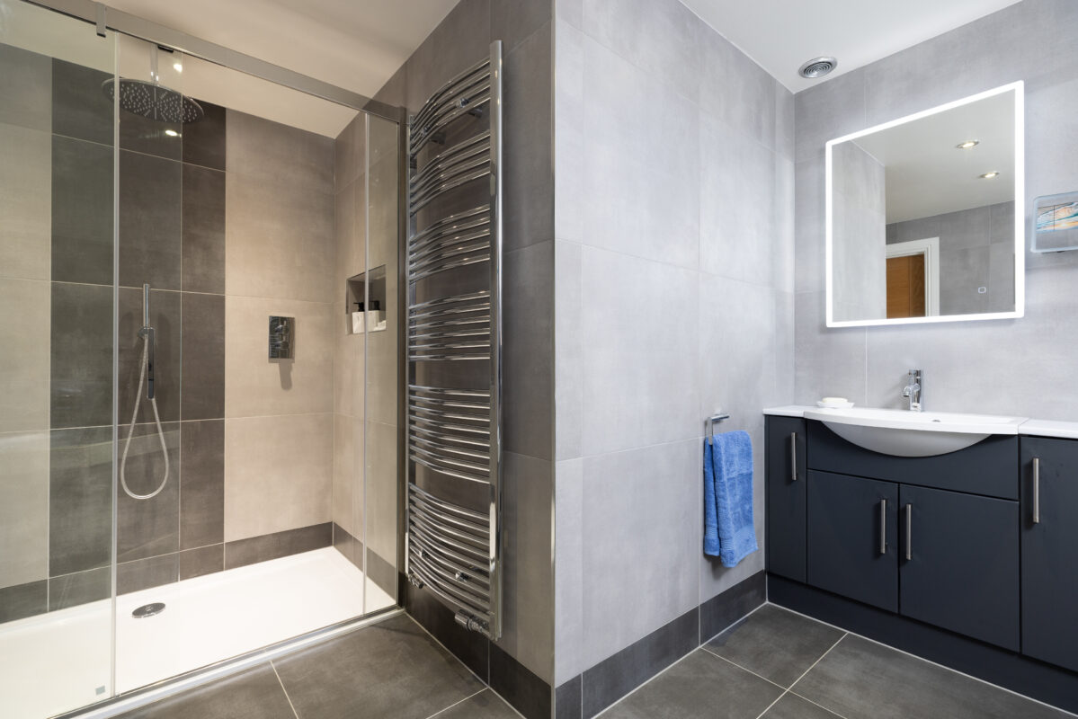 A modern bathroom renovation in Perthshire that features a shower area with an overhead rain shower, along with fitted bathroom furniture consisting of a wash basin and mirror.