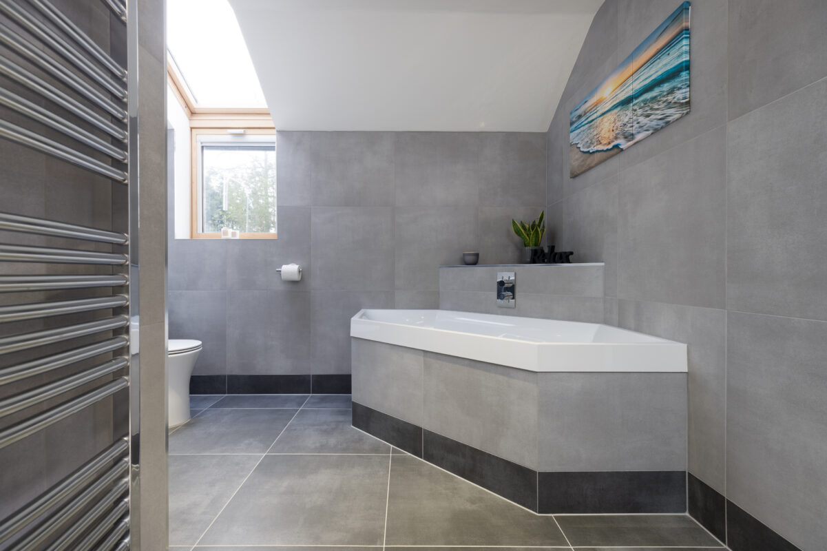 A hexagonal built-in bath located in a fully tiled bathroom in Perthshire, featuring a bulkhead for storage, and a heated towel rail.