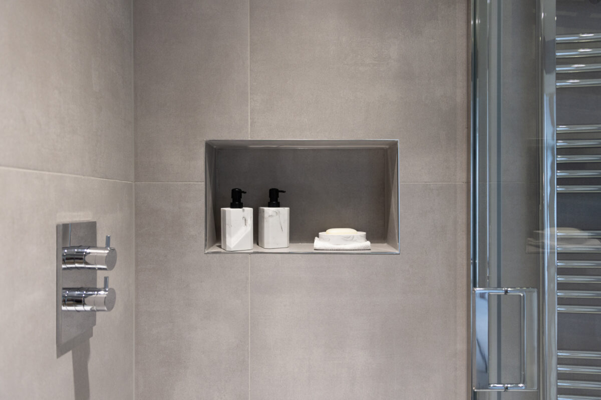 A recessed shelf in the shower area with two shampoo bottles and chrome bathroom fixtures.
