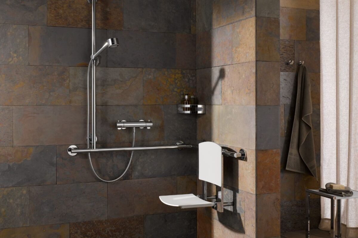 Accessible bathroom featuring full stone tiling, a foldable seat, and a grab bar.