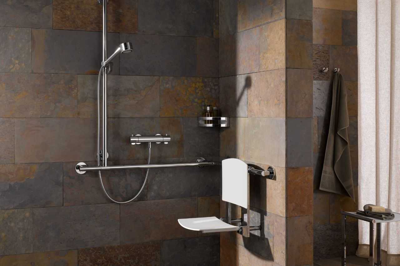 Accessible bathroom featuring full stone tiling, a foldable seat, and a grab bar.