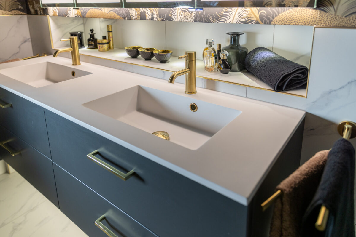 A double vanity with a wash basin, gold taps, drawers with brass handles, and a recessed shelf with lighting.