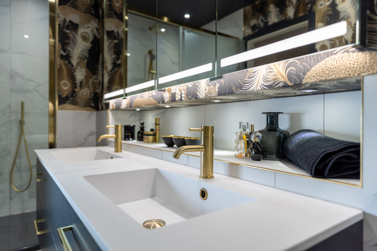 A double vanity with white countertops, a gold mixer, and leopard-patterned wallpaper, complete with a mirrored cabinet, in an ensuite bathroom renovation in Edinburgh.
