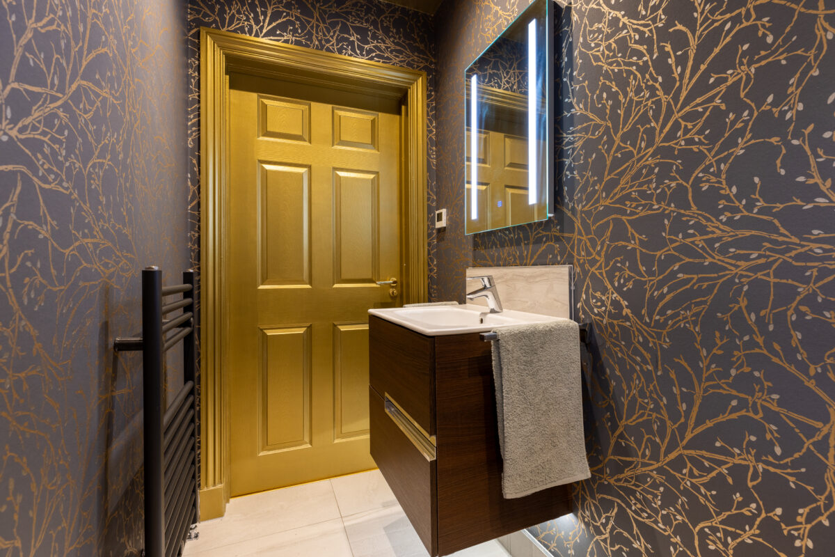 Cloakroom featuring a matte black vertical towel rail, a mounted vanity unit, and an illuminated mirror cabinet. vanity unit, an