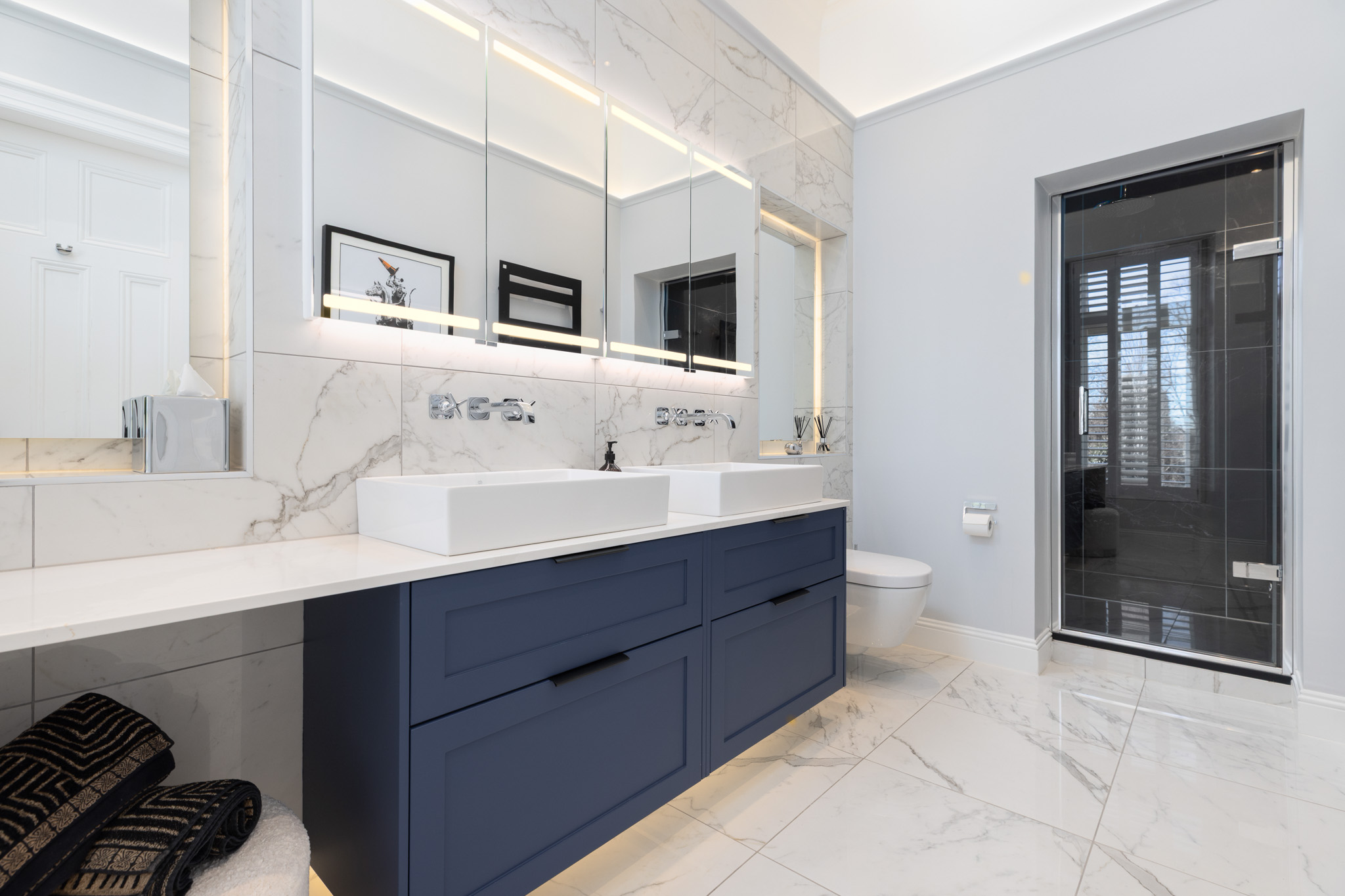 Luxury bathroom with double vanity, large mirror cabinet with LED lighting, marble walls and floors, and a glass steam room.