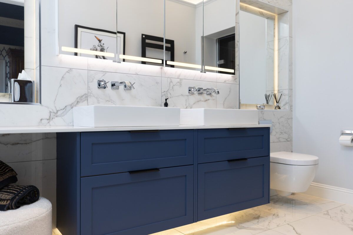 Modern ensuite with steam room featuring a two drawer navy blue vanity unit, double basins, marble walls and floors, and under-cabinet LED lighting.