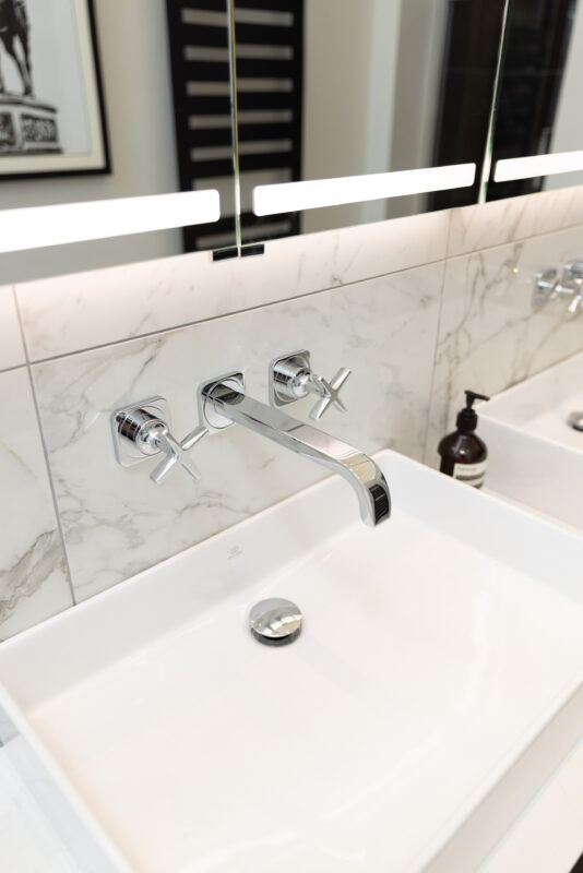 Modern chrome wall-mounted tap with cross handles over a rectangular basin and marble backsplash.