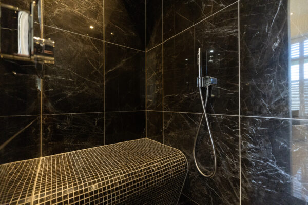 Modern steam shower with dark marble tiles, handheld showerhead, and curved tiled bench.
