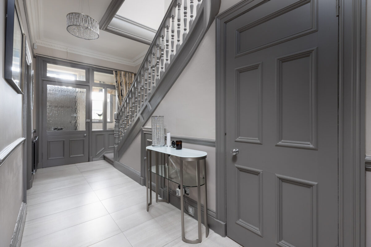 Elegant hallway with grey panelled walls, staircase, tiled flooring, and a glass console table in a newly renovated home