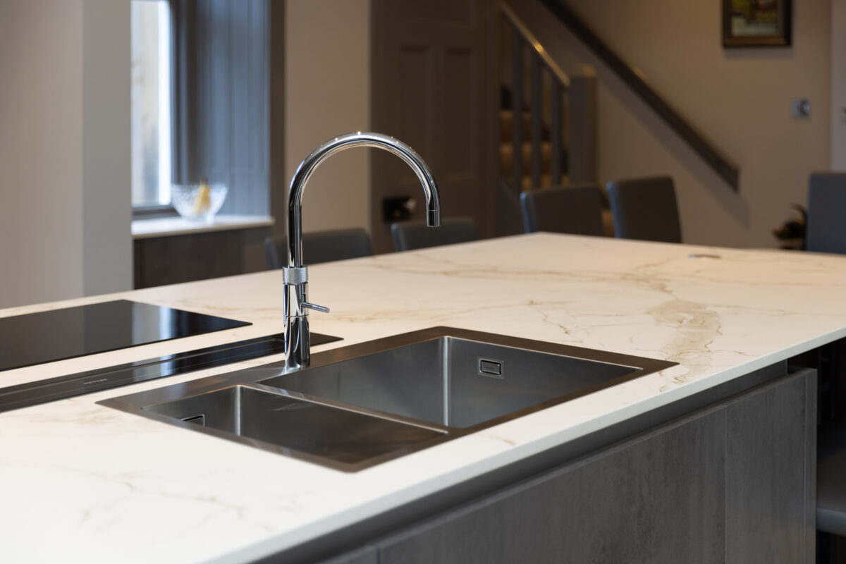 Modern kitchen island with marble countertop, built-in stainless steel sink, chrome quooker tap, and induction cooktop in a newly renovated kitchen.