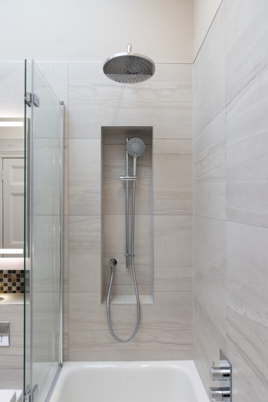 A fully tiled bath area with a shower system. A recess is created with the installation of the handheld shower.