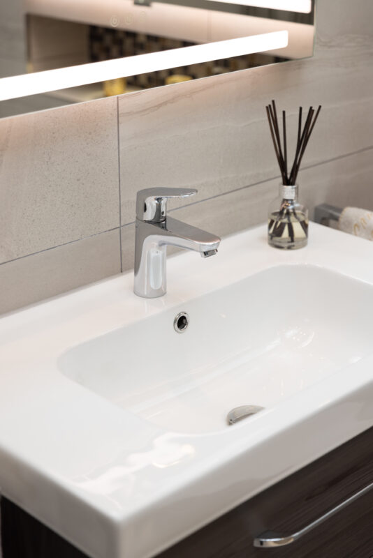 Close-up of a modern white bathroom basin with a chrome mixer and diffuser