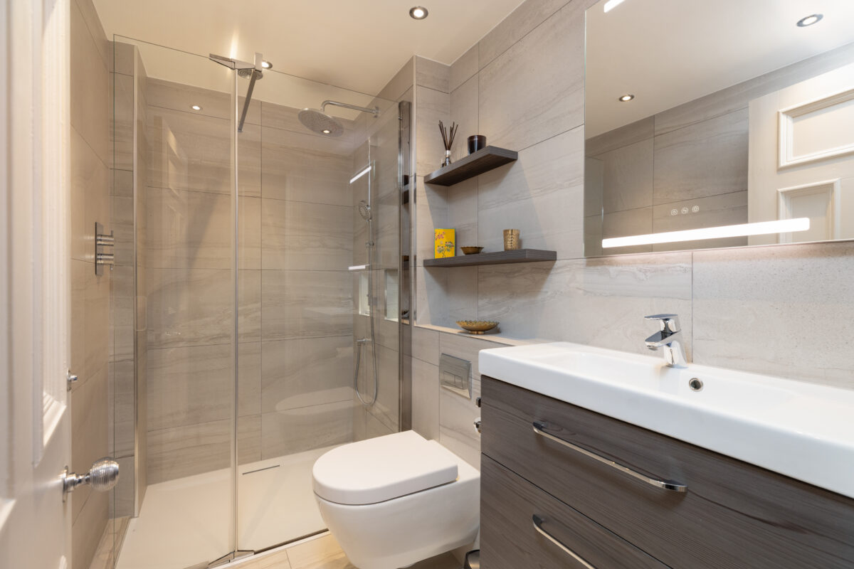 modern bathroom with a walk-in shower, wall-mounted toilet, wood vanity unit, and floating shelves with decorative items as part of a whole home renovation.
