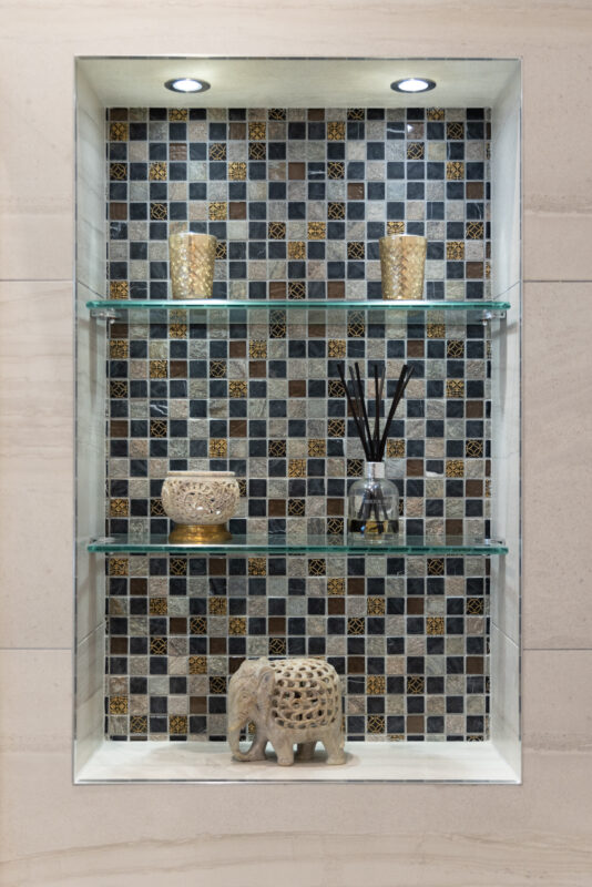 Recessed wall with mosaic tile background, glass shelves, and decorative items in a newly renovation bathroom