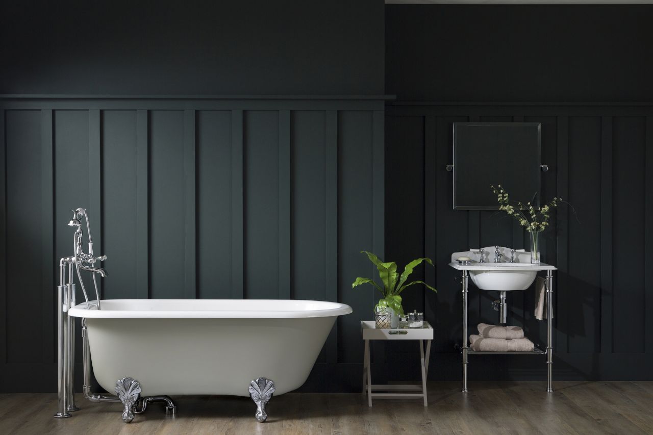 A large free-standing traditional bathroom with fixtures in chrome finish. The space also features a washstand and a square mirror.