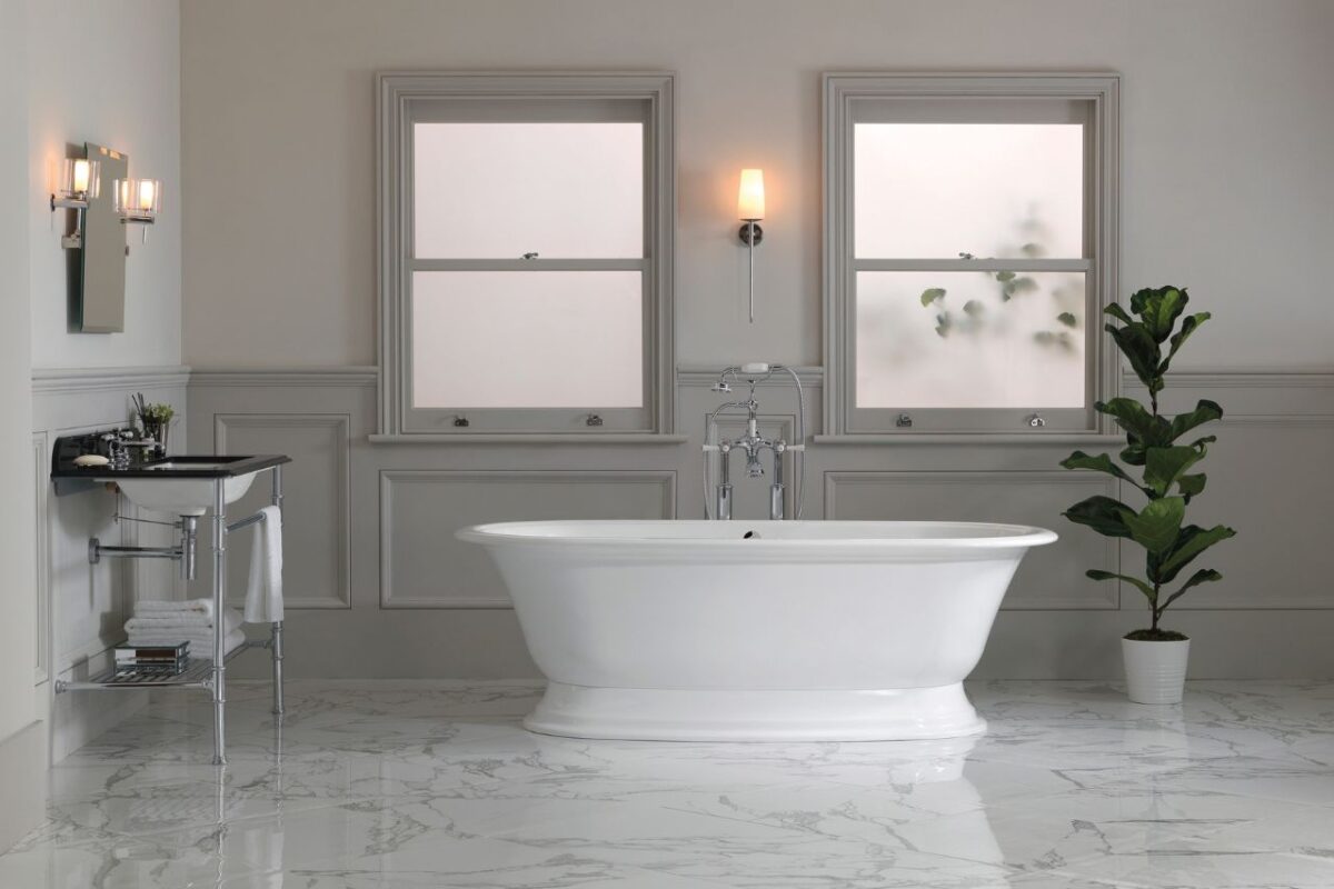 A spacious bathroom features a classic washbasin. Above it, there is a mirror flanked by two wall-mounted lights. A freestanding bath with a floor-mounted mixer is positioned at the centre of the room. The bathroom is panelled to create a sleek, elegant appearance.