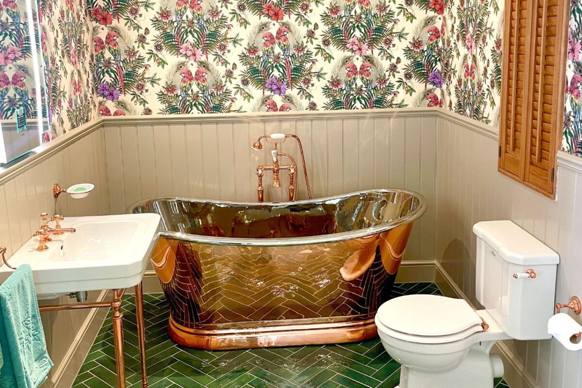 A traditional-style bathroom with wallpaper adding style and uniqueness to the space. The bathroom features a freestanding bath and fixtures with a copper finish.