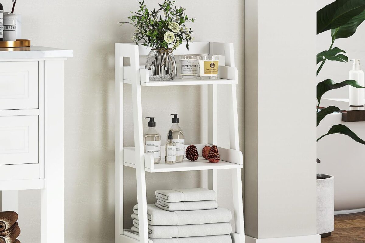 A white wooden ladder shelf unit with three tiers holds towels, soap dispensers, and candles, serving as a clever bathroom storage solution.