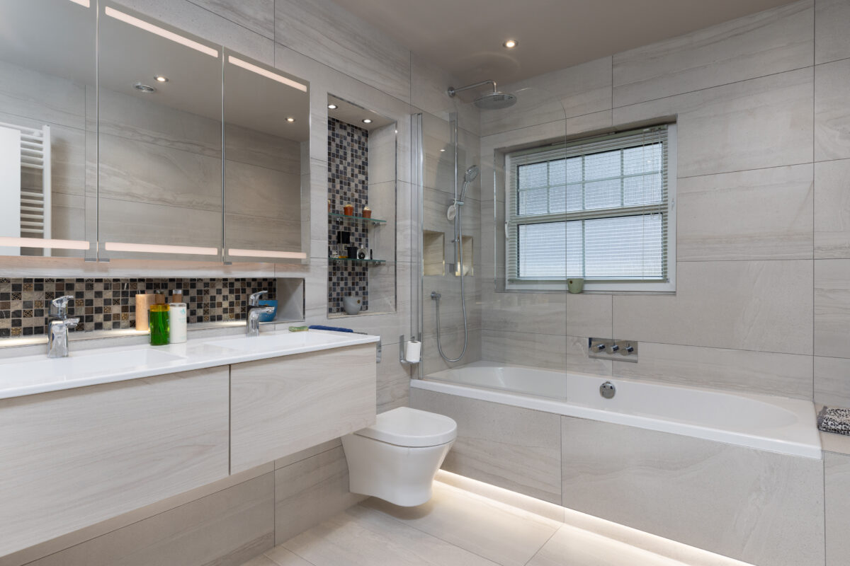 A built-in bath with a shower panel and recessed shelves to complete the bath area. A large vanity with a three-door mirror cabinet and WC area as part of an entire home renovation.