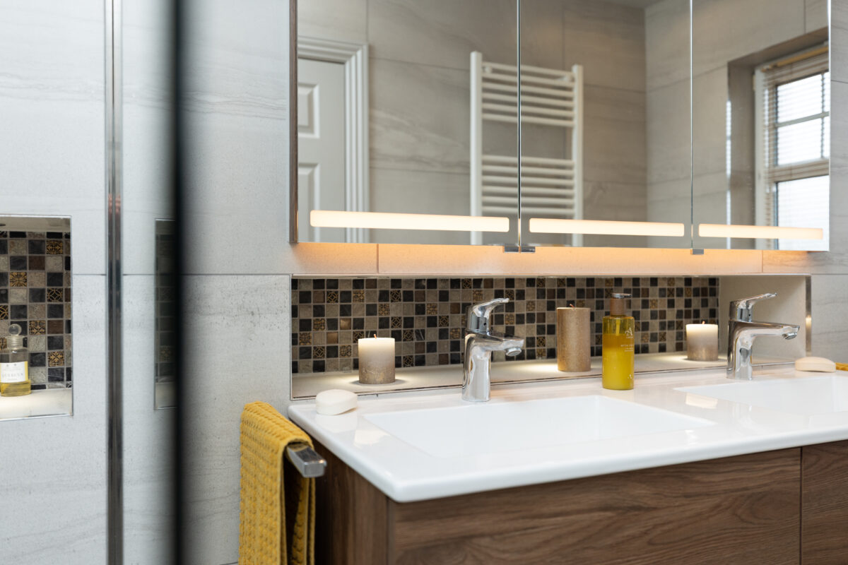 A dual basin with a three-door LED mirror cabinet and a mosaic tile recess in an ensuite bathroom.