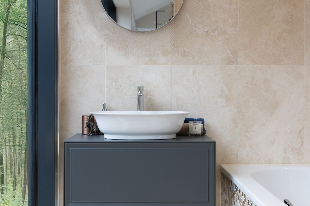 A stone-tiled splashback with a washbasin sitting on a grey bathroom vanity unit.