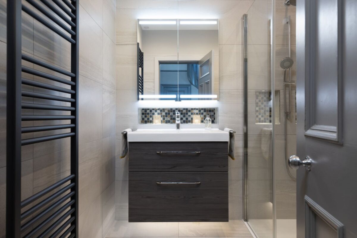 A recessed splashback with mosaic tiles adds a luxurious touch to the space. An LED mirror cabinet is mounted above the vanity unit.