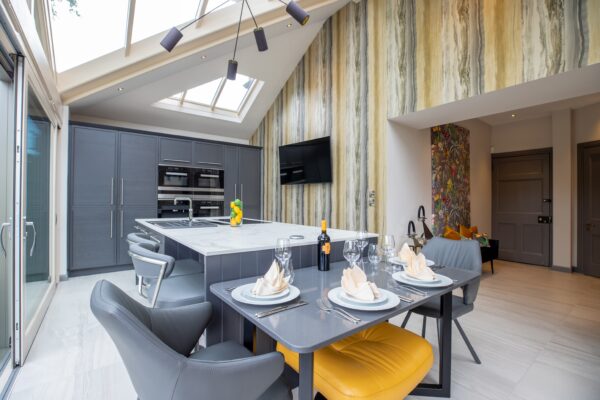 Modern kitchen installation featuring sleek cabinetry, a central island, and a dining area. The design is enhanced with patterned wallpaper and a large heated towel rail.
