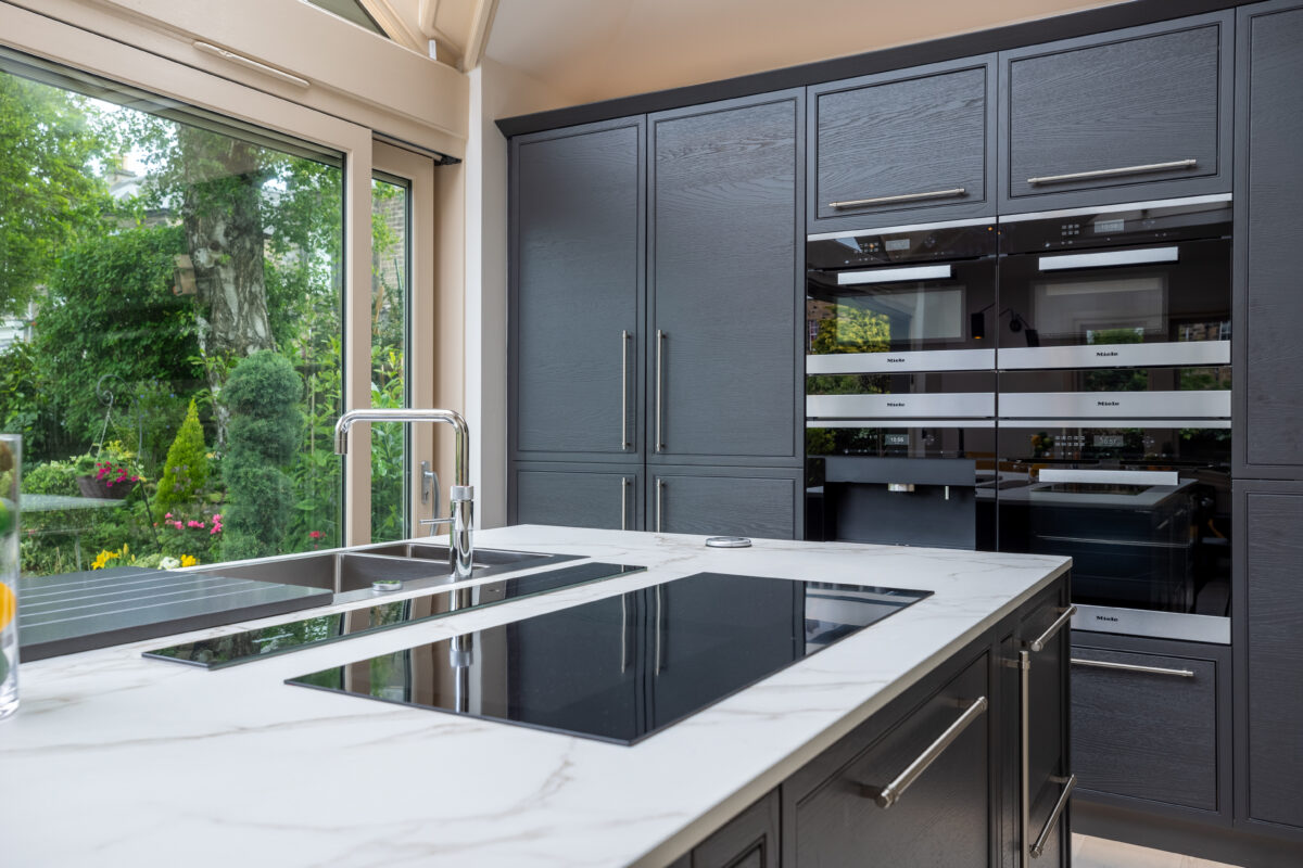 Grey kitchen cabinetry with chrome handles and integrated Miele appliances, featuring a stone-topped island as part of a kitchen extension in Edinburgh.