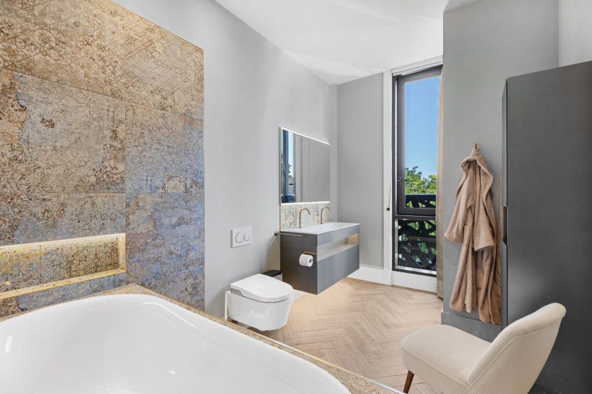 A modern spacious master ensuite with a vanity with dual wash basin and taps. Above the tiles is a recessed mirror.