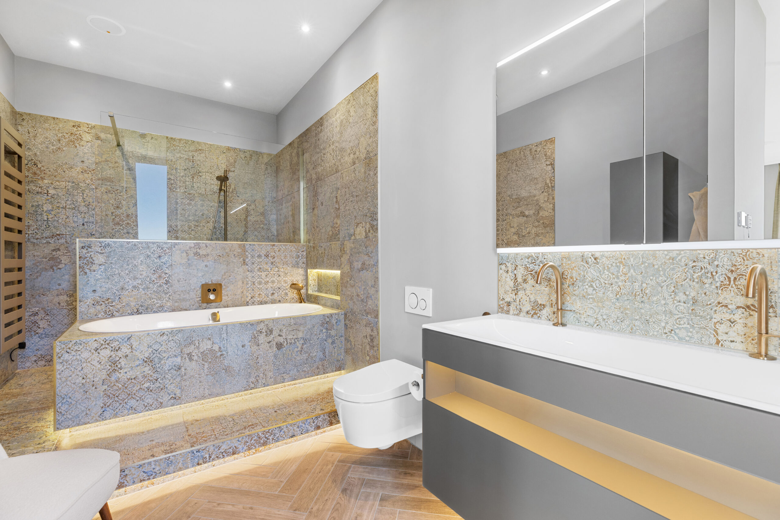 A modern bathroom installation with brushed bronze fixtures, separate bath and shower area, a large mirror cabinet, and vanity.
