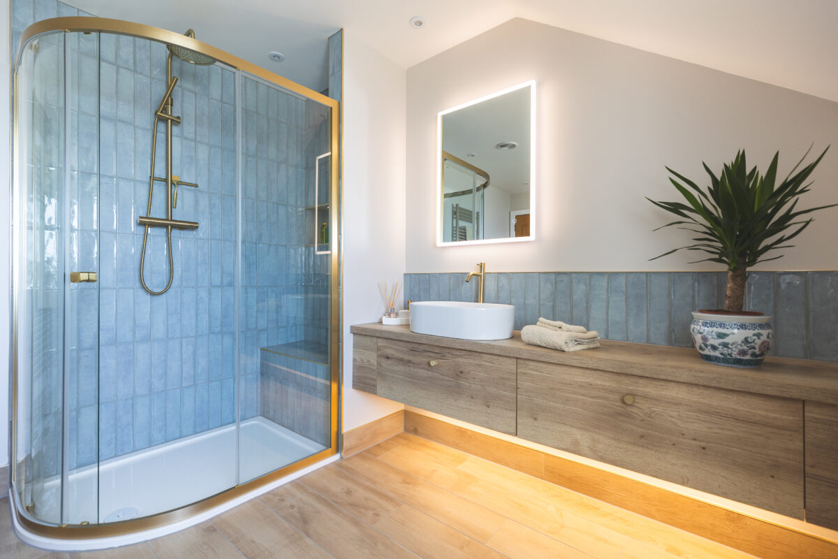 A spacious bathroom fitting which features brushed brass fixtures, a large shower area, and a vanity unit.