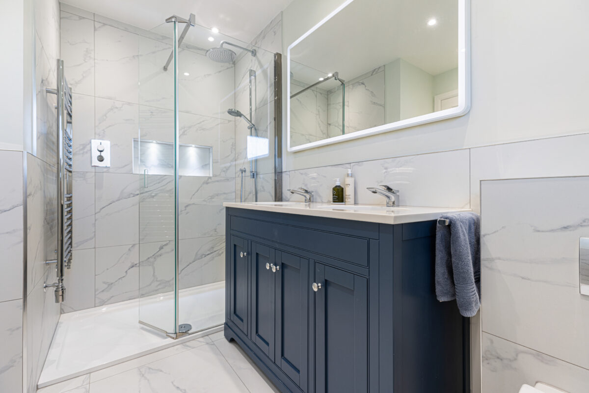 Spacious shower room with a fully tiled shower and recess, and a large mirror above a dual-basin vanity, part of a bathroom and en-suite renovation in Edinburgh.